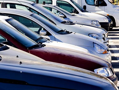 Row of cars with three blurry adults standing in the background.